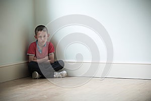 Unhappy Child Sitting In Corner Of Room