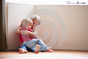 Unhappy Children Sitting On Floor In Corner At Home