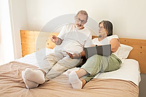 Unhappy confused senior caucasian couple lie on bed, pay for bills, taxes in bedroom interior