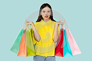 Unhappy consumer, unpleased young woman with shopping bags at blue background
