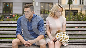 Unhappy couple sitting after fight, girl with flowers, problem in relationship