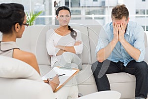 Unhappy couple sitting on sofa at therapy session