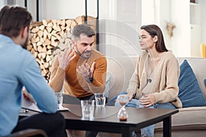 Unhappy couple sitting on sofa at therapy session in therapists office