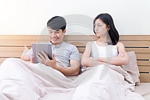 Unhappy couples at home. Handsome using tablet ignoring his girlfriend feeling unsatisfied in the bedroom. Couple having