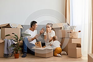 Unhappy crazy angry man screaming on his wife while sitting with her near sofa on floor, couple having argument in their new