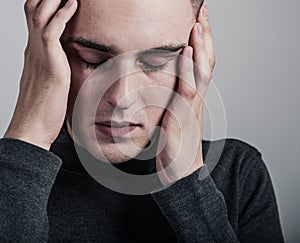 Unhappy crying ill man with headache holding the head. Closeup studio portrait on grey background. Negative problem concept