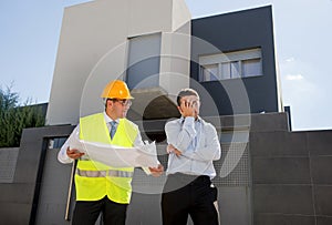 Unhappy customer in stress and constructor foreman worker with helmet and vest arguing outdoors on new house building blueprints