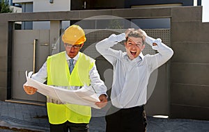 Unhappy customer in stress and constructor foreman worker with helmet and vest arguing outdoors on new house building blueprints