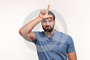 Unhappy depressed man with beard in blue shirt holding hand near forehead showing loser gesture with fingers, having financial and