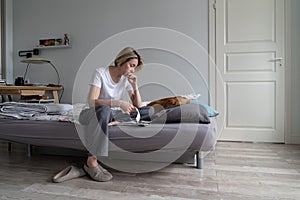 Unhappy depressed middle-aged woman living alone with dog sits on bed counting bills