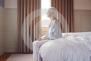 Unhappy And Depressed Senior Woman Sitting On Edge Of Bed At Home