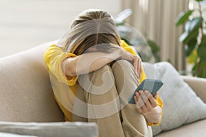 Unhappy, despaired crying millennial caucasian blond female with smartphone suffering from depression