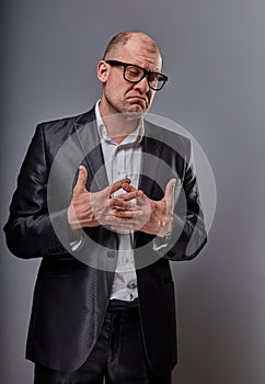 Unhappy doubt busuness man in black suit and glasses showing the palm refusing sign on grey background. Closeup