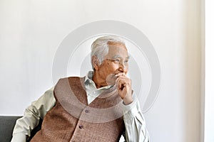 Unhappy elderly asian man with carefully thought gesture, Lonely old man looking out the window worry about life problem.