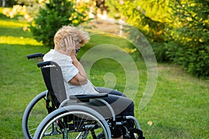 Unhappy elderly woman crying while sitting in a wheelchair on a walk outdoors.