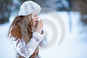 unhappy elegant female warming cold hands with breath