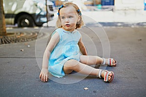 Unhappy and emotional toddler girl sitting on the ground outdoors