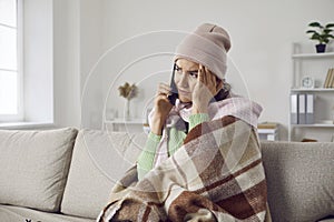 Unhappy and exhausted woman with cold symptoms sitting at home calls her doctor or ambulance.