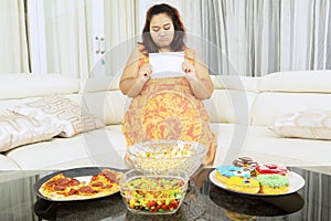 Unhappy fat woman hold blank paper near junk foods