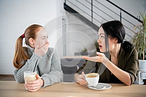 Unhappy female friends discuss shocking news. Two shocked young women covering mouth and looking at each other at cafe
