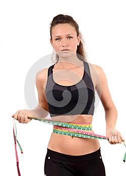 Unhappy fit girl measuring her waist with three measuring tapes.