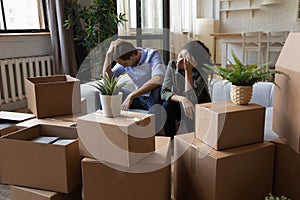 Unhappy frustrated couple sitting on couch with cardboard boxes, eviction