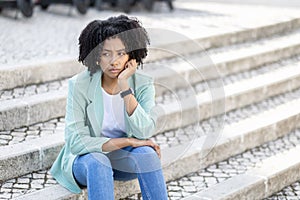 Unhappy frustrated pensive millennial black woman sitting on street