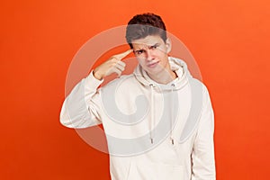 Unhappy frustrated young man in casual hoodie and stylish hairdo showing stupid gesture, does not believe in his strengths and