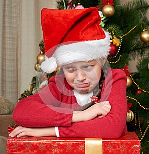 Unhappy girl crying near christmas tree, dressed in red and santa hat