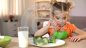 Unhappy girl eating healthy but tasteless food, broccoli lying on table, diet