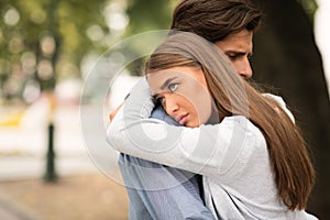 Unhappy Girl Hugging Unloved Boyfriend Standing Outdoors In Park