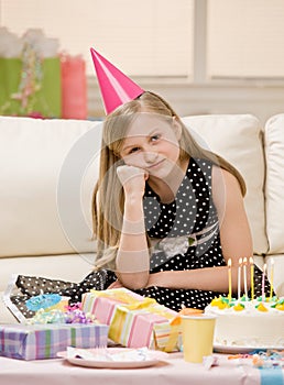 Unhappy girl in party hat sits with gifts