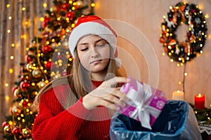 Unhappy girl in Santa hat throwing present away to the recycle bin