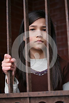 Unhappy girl standing behind bars