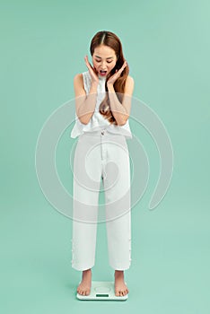 Unhappy girl standing on weight scale over blue background