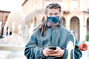 Unhappy guy with protective mask using tracking app on mobile smartphone - Young worried millenial sharing content on social media
