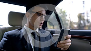 Unhappy handsome businessman reading bad news on smartphone, ride in luxury auto