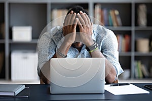 Unhappy hopeless African American man holding head in hands