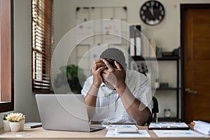 Unhappy hopeless African American man holding head in hands, overwhelmed tired businessman sitting at work desk with