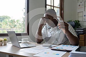 Unhappy hopeless African American man holding head in hands, overwhelmed tired businessman sitting at work desk with