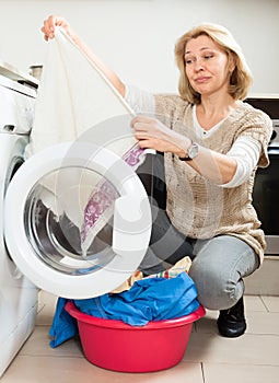 Unhappy housewife with clothes near washing machine