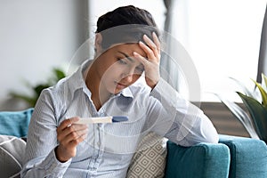 Unhappy Indian woman looking at pregnancy test, upset by result