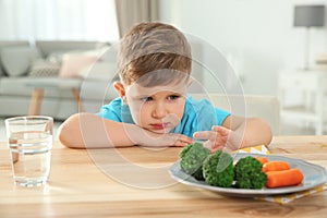 Unhappy little boy refusing to eat vegetables at table