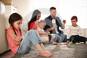 Unhappy little girl feeling jealous while parents spending time with other children