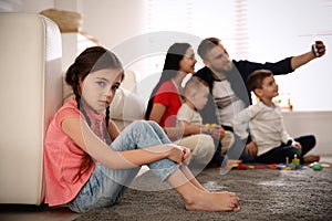 Unhappy little girl feeling jealous while parents taking selfie with other children