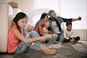 Unhappy little girl feeling jealous while parents taking selfie with other children