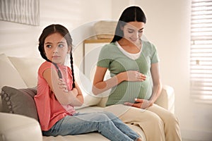 Unhappy little girl near pregnant mother. Feeling jealous towards unborn sibling