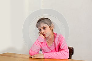 Unhappy little girl nine years old sitting at table