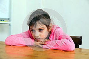 Unhappy little girl nine years old sitting at table