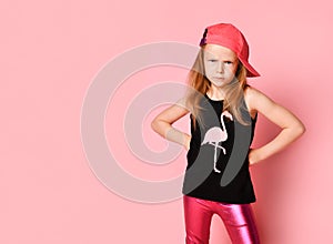 Unhappy little girl standing with hands on hips and bending brows looking at camera. Three quarter length portrait isolated on